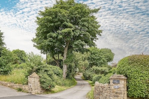 A rural road leading to a stone gate with a sign indicating 'Baiting Court'. - Host Stay The Cottage Barn (Keighley)