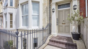 Une maison de ville dotée d’une baie vitrée, d’une porte d’entrée avec une plaque de numéro et d’un petit jardin agrémenté d’une plante en pot.