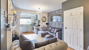 Un salon moderne avec un canapé gris, un coin repas avec une cuisine en arrière-plan et une grande porte blanche.