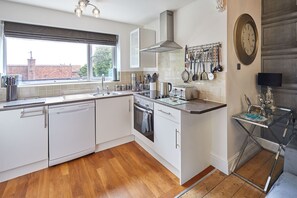 A modern kitchen with white cabinetry, a stainless steel range hood, a window with blinds, and a wall-mounted clock. - Host Stay Apartment 2 15 Prospect Hill (Whitby)