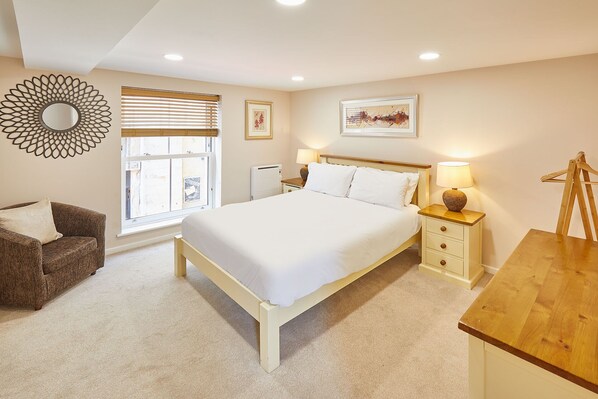 A bedroom with a large bed, a wooden nightstand, a chair, a desk, and a decorative wall piece. - Host Stay Lobster Pot Apartment (Whitby)