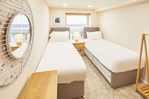 A hotel room with two single beds, a wooden nightstand, a mirror with decorative elements, and a window with blinds. - Host Stay Lobster Pot Apartment (Whitby)