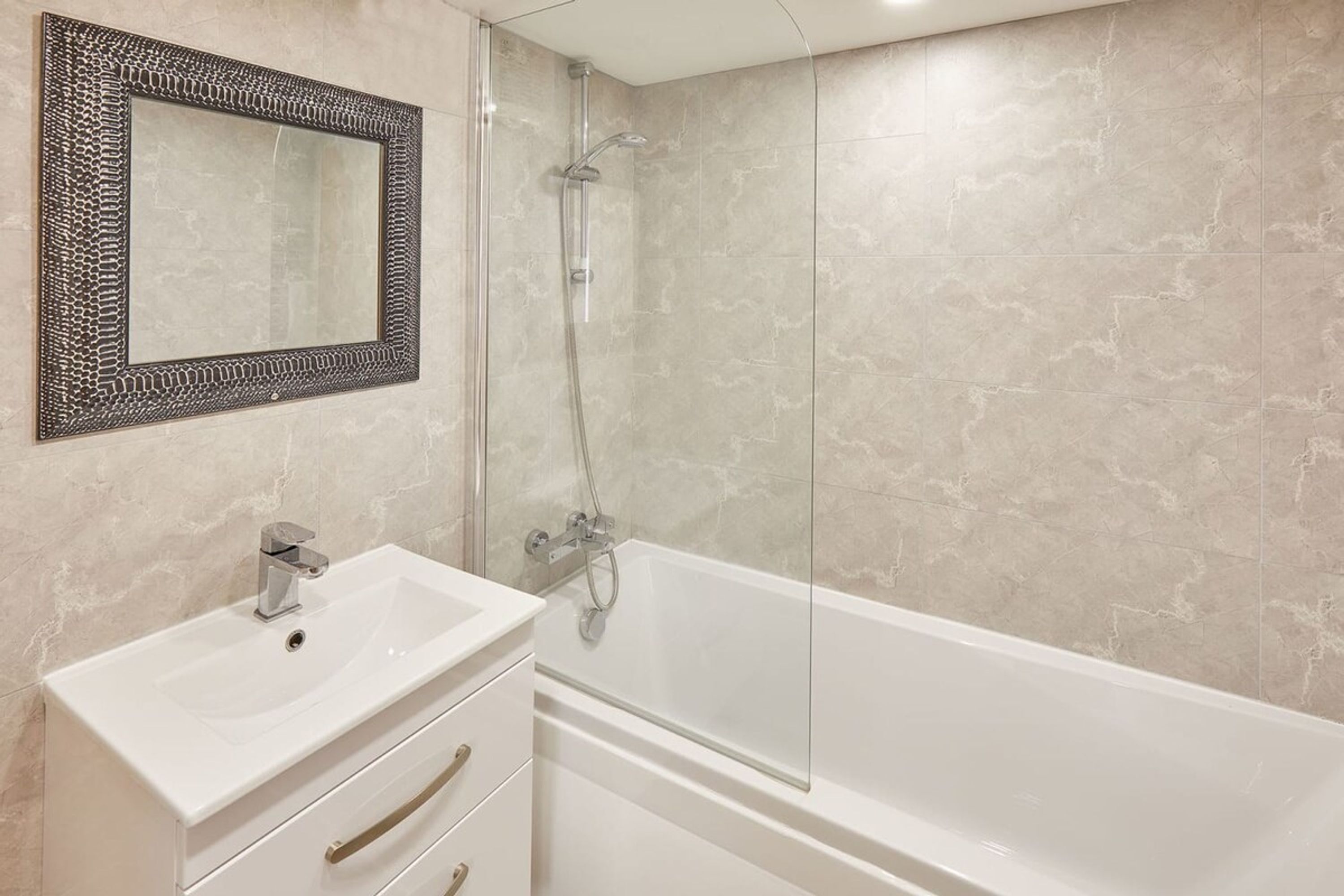 A bathroom with a white sink, a mirror with a decorative frame, and a glass-enclosed shower.