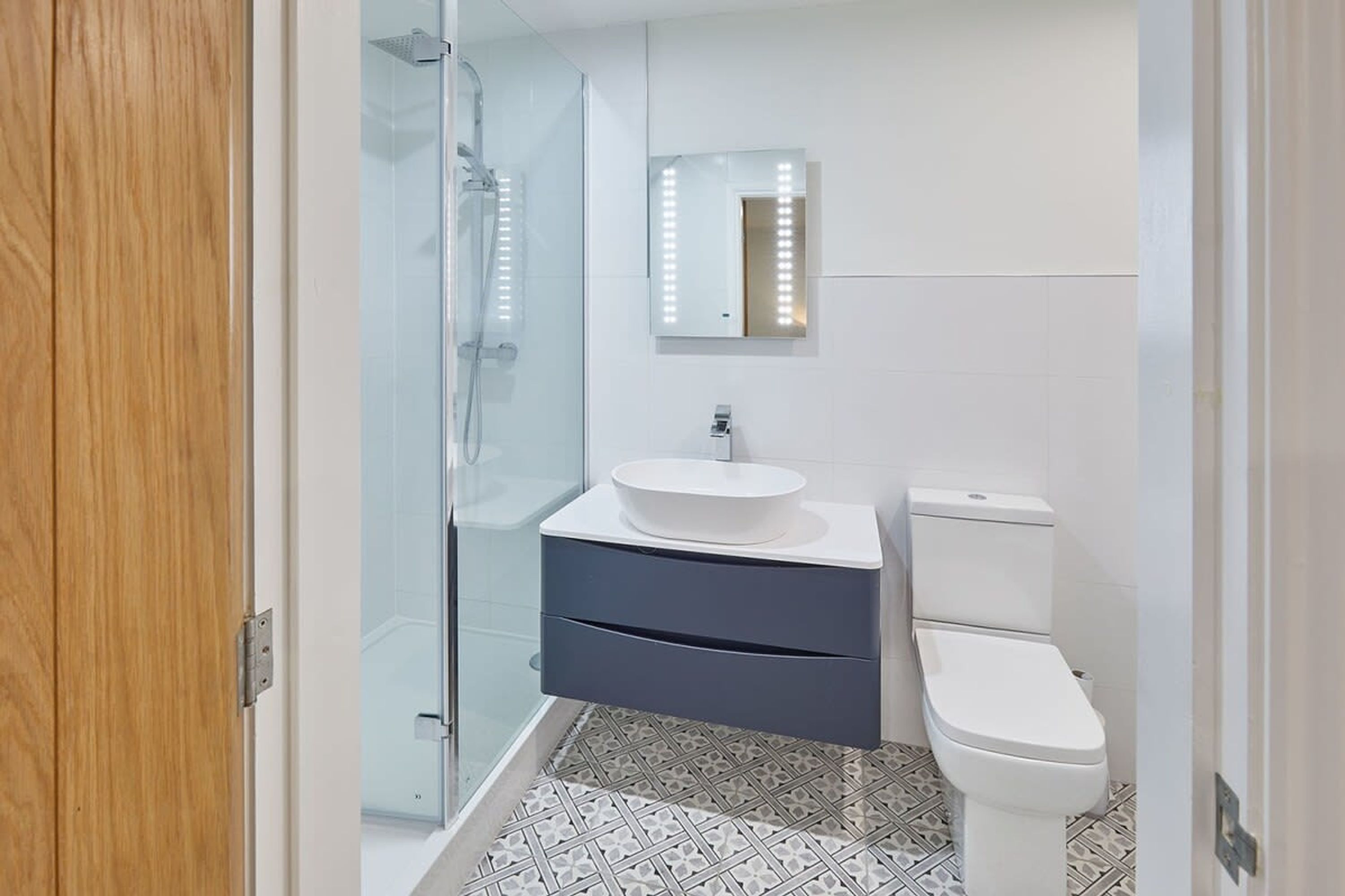 A bathroom with a glass shower enclosure, a white sink, a dark blue vanity, and a white toilet.