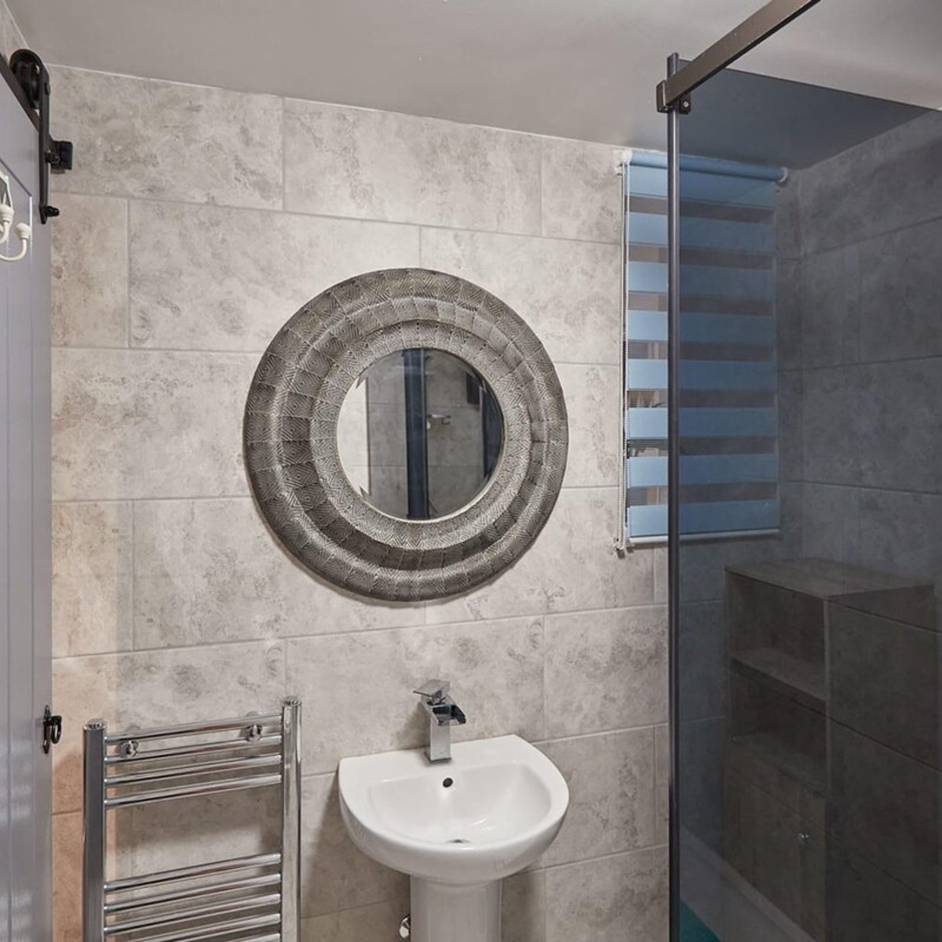 A bathroom with a round mirror, a white sink, and a glass shower enclosure.
