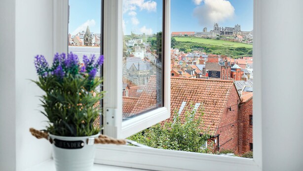 A view from a window overlooking a historic town with red-roofed buildings, a prominent church, and a sign for the George Hotel. - Host Stay Captain s Retreat (Whitby)
