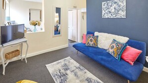 A modern living room with a blue sofa, a flat-screen TV, and a decorative rug. - Host Stay Ocean Wave (Scarborough)