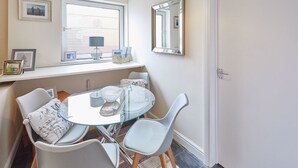 A dining area with a glass table, white chairs, a window with blinds, a mirror, and framed pictures on the wall. - Host Stay Ocean Wave (Scarborough)