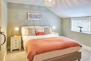 A bedroom with a bed, two bedside lamps, a nightstand, a window with blinds, and a wall-mounted picture.