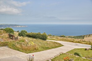 A coastal path with a bench, grassy areas, and a view of the sea.