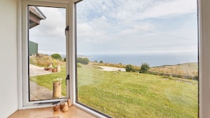 Una habitación con un amplio ventanal corredero que da a un espacio exterior con césped y vistas al mar.