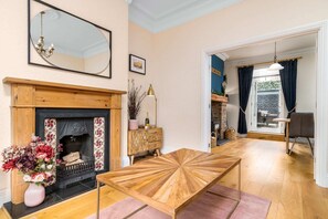 A living room with a fireplace, a mirror, a wooden coffee table, and a view into the dining area. - Host Stay Railman s Rest (Whitby)