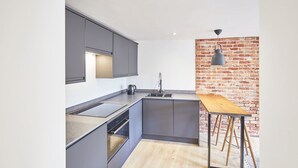 A modern kitchen with grey cabinets, a wooden table, and a brick wall. - Host Stay Modern Industrial Golden Lion Apartments (Whitby)
