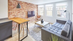 A modern living room with a brick wall, a flat-screen TV, a wooden table, a grey sofa, and large windows. - Host Stay Modern Industrial Golden Lion Apartments (Whitby)