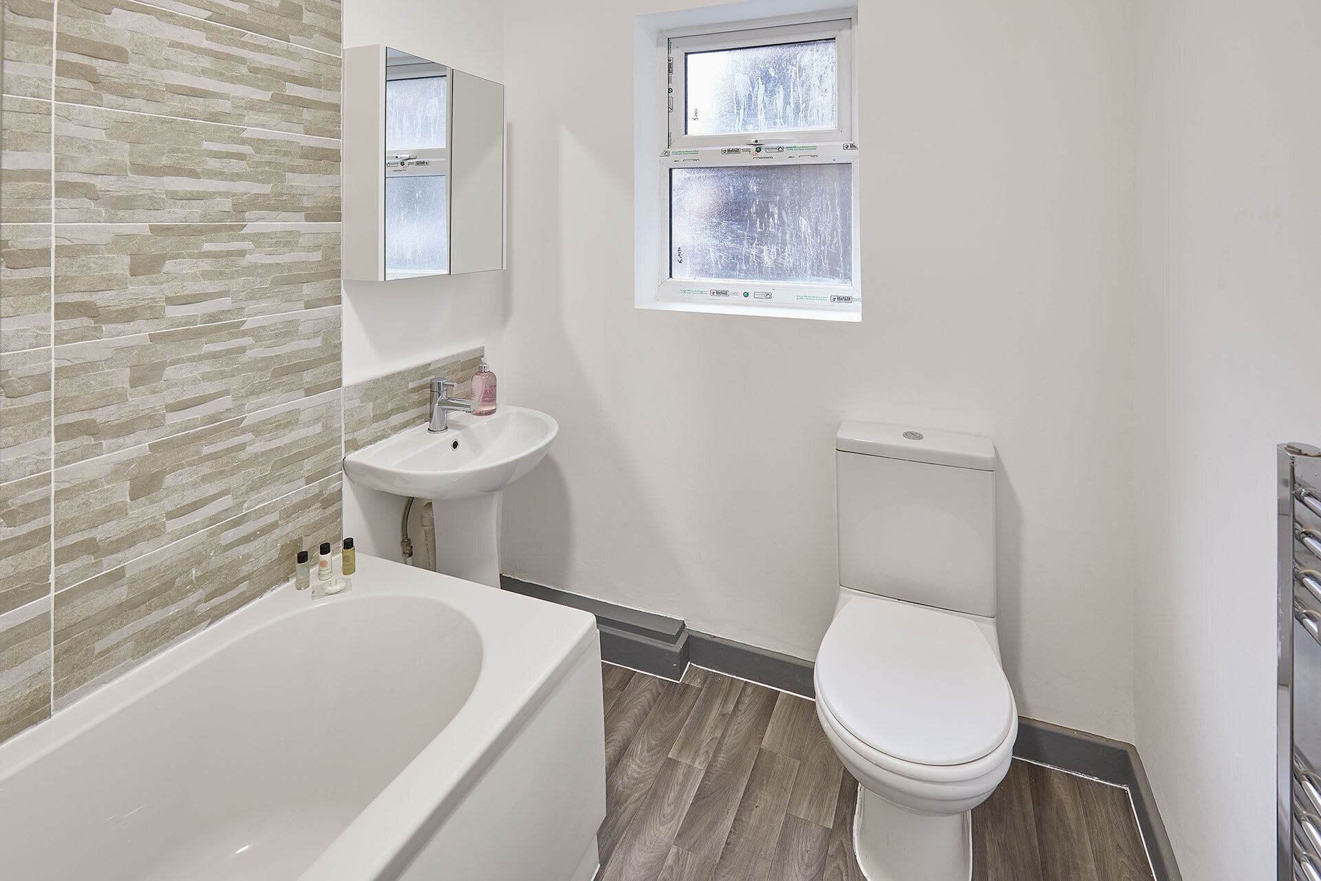 Un baño con bañera, lavabo, inodoro y una ventana con vidrio esmerilado.