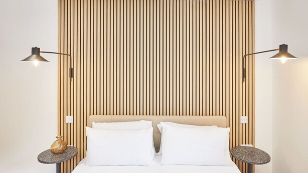 A neatly made bed with white linens, flanked by two bedside tables with lamps, against a backdrop of vertical wooden slats. - Host Stay Simply Scandi Golden Lion Apartments (Whitby)