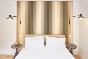 Una cama bien hecha con sábanas blancas, flanqueada por dos mesitas de noche con lámparas, sobre un fondo de listones de madera verticales.