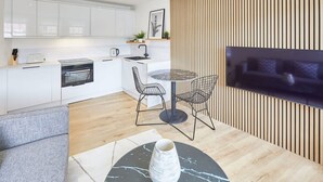 A modern kitchen with white cabinets, a built-in oven, and a dining area with a round table and chairs. - Host Stay Simply Scandi Golden Lion Apartments (Whitby)