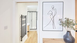 A hallway with a radiator, a framed abstract artwork, and a potted plant on a wooden table. - Host Stay Simply Scandi Golden Lion Apartments (Whitby)