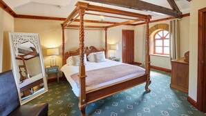 Een traditioneel hemelbed met houten frame en baldakijn, een grote spiegel met versierde lijst, en een kamerbreed tapijt met dessin.