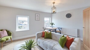 A modern living room with a grey sofa, a dining table, and a view of the city through large windows. - Host Stay Whitby Heights (Whitby)