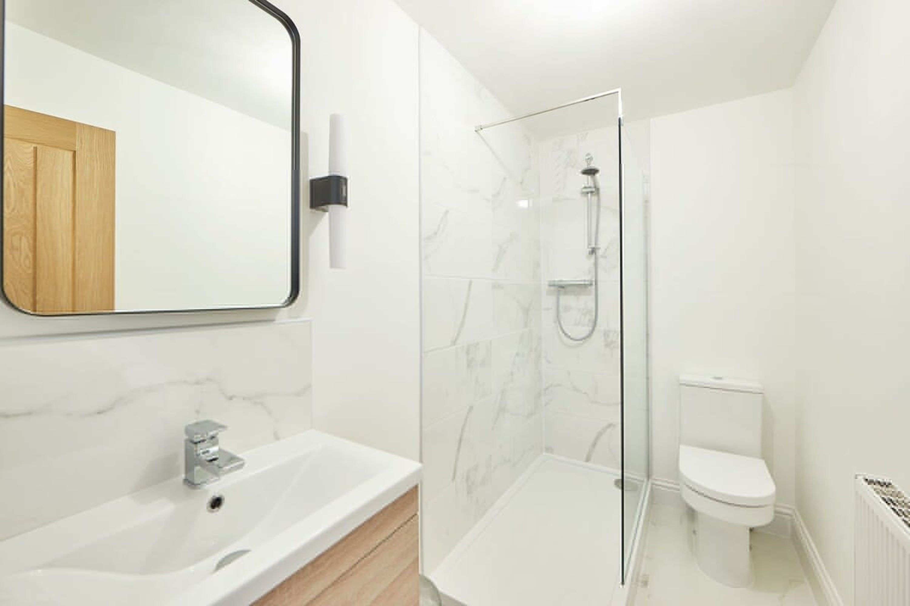 A modern bathroom with a white marble sink, a glass-enclosed shower, and a toilet.