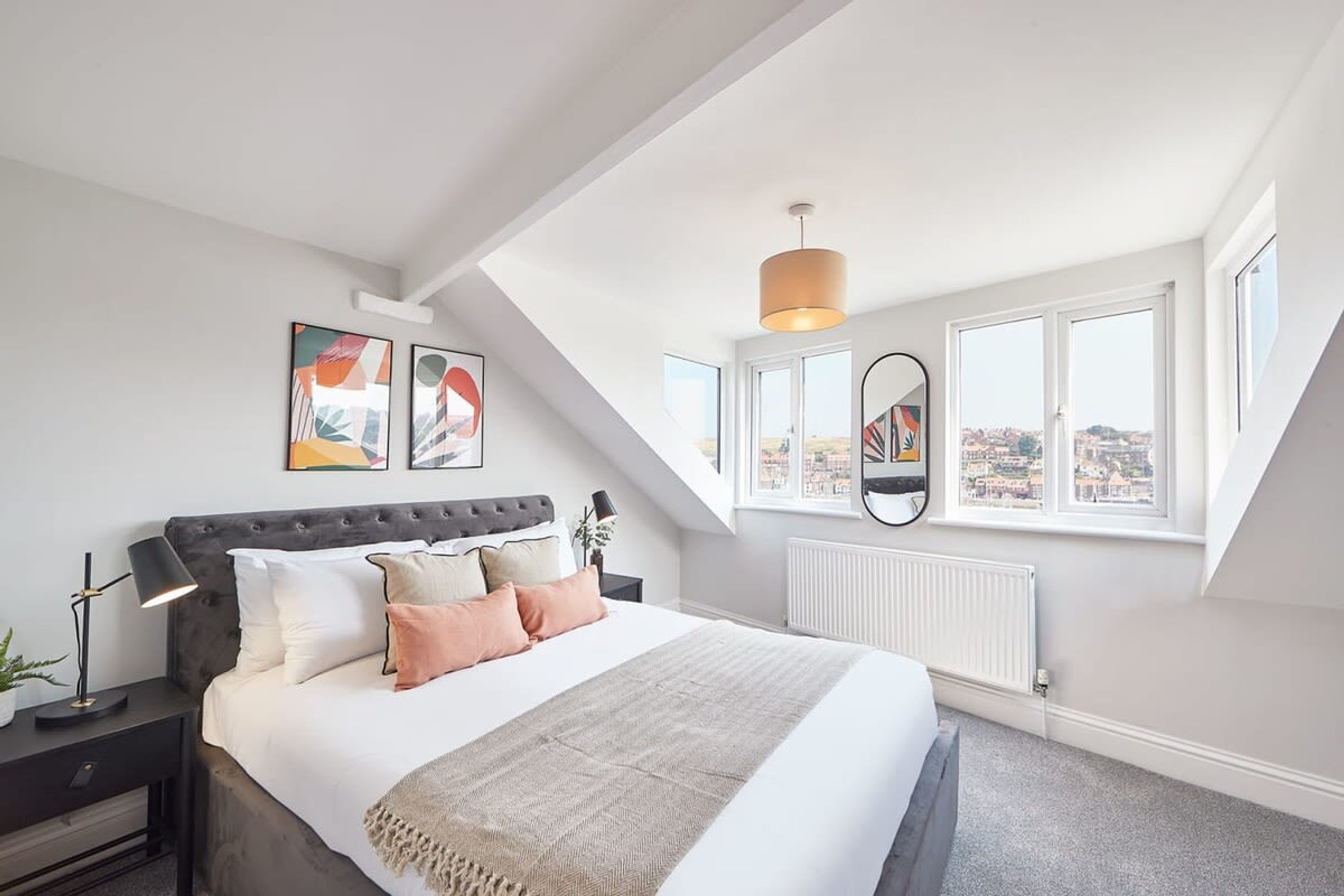 Een slaapkamer met een groot bed, nachtkastje, lamp en een raam met uitzicht op de stad.