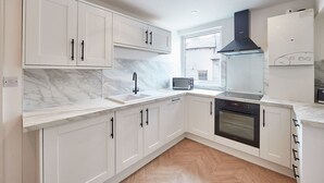 A modern kitchen with white cabinets, a marble countertop, a black range hood, a built-in oven, and a window providing natural light. - Host Stay Whitby Heights (Whitby)