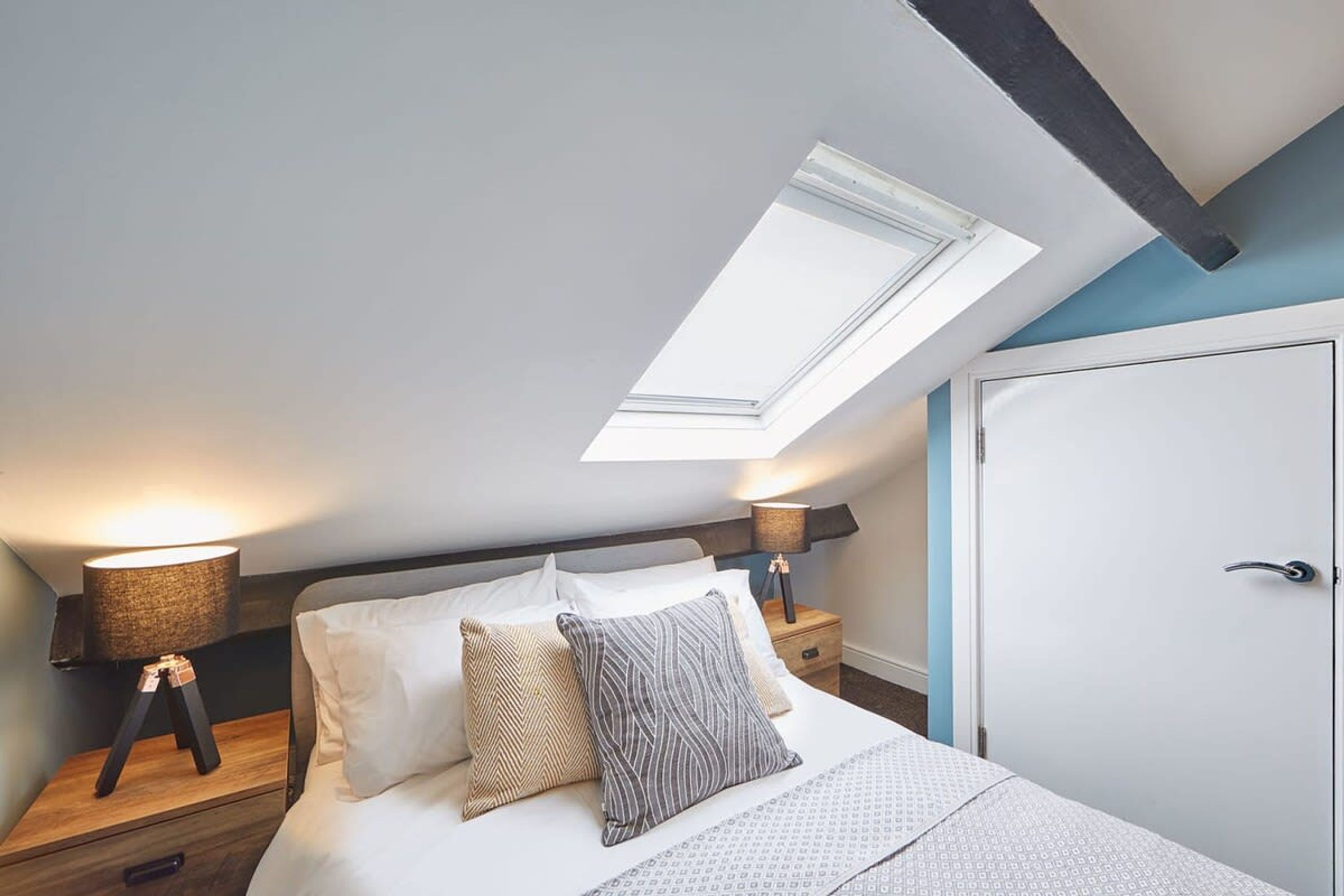 Un dormitorio con tragaluces, una cama con almohadas estampadas, lámparas de noche y una puerta.