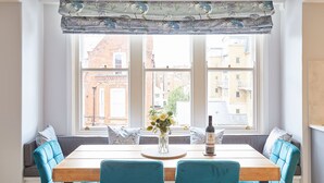 A dining area with a wooden table, teal upholstered chairs, and a window with a patterned valance. - Host Stay The Avenue Victoria Apartment (Scarborough)