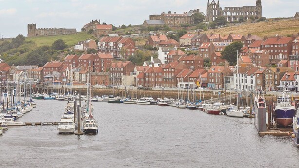 A harbor with boats docked, a historic building on a hill, and residential buildings in the foreground. - Host Stay Starboard Bow (Whitby)