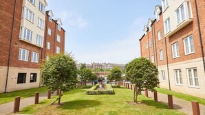A courtyard with two brick apartment buildings, a central lawn, and trees. - Host Stay Starboard Bow (Whitby)