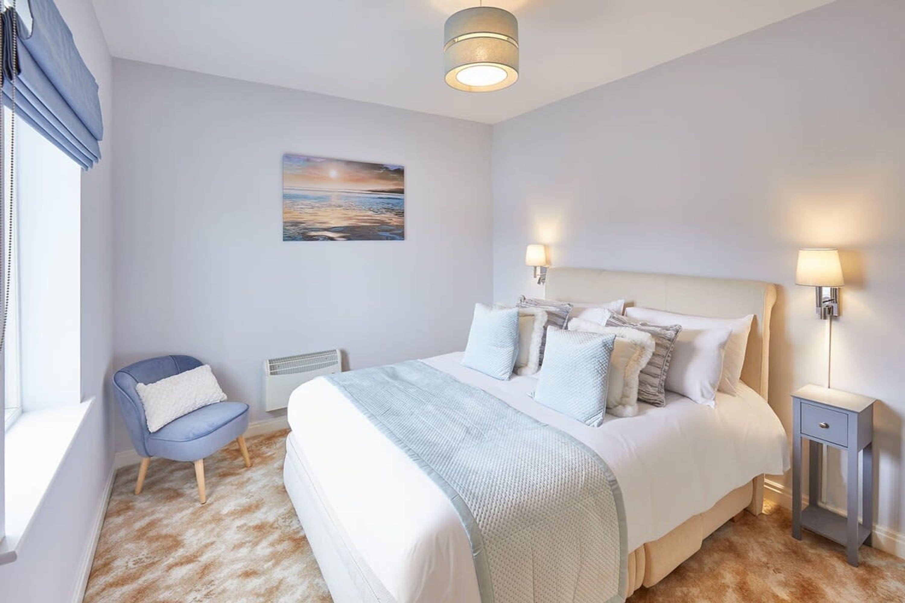 A bedroom with a large bed, a chair, a bedside table, and a wall-mounted lamp.