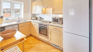 A modern kitchen with wooden cabinets, a stainless steel oven, a microwave, and a large window providing a view of the city. - Host Stay Starboard Bow (Whitby)