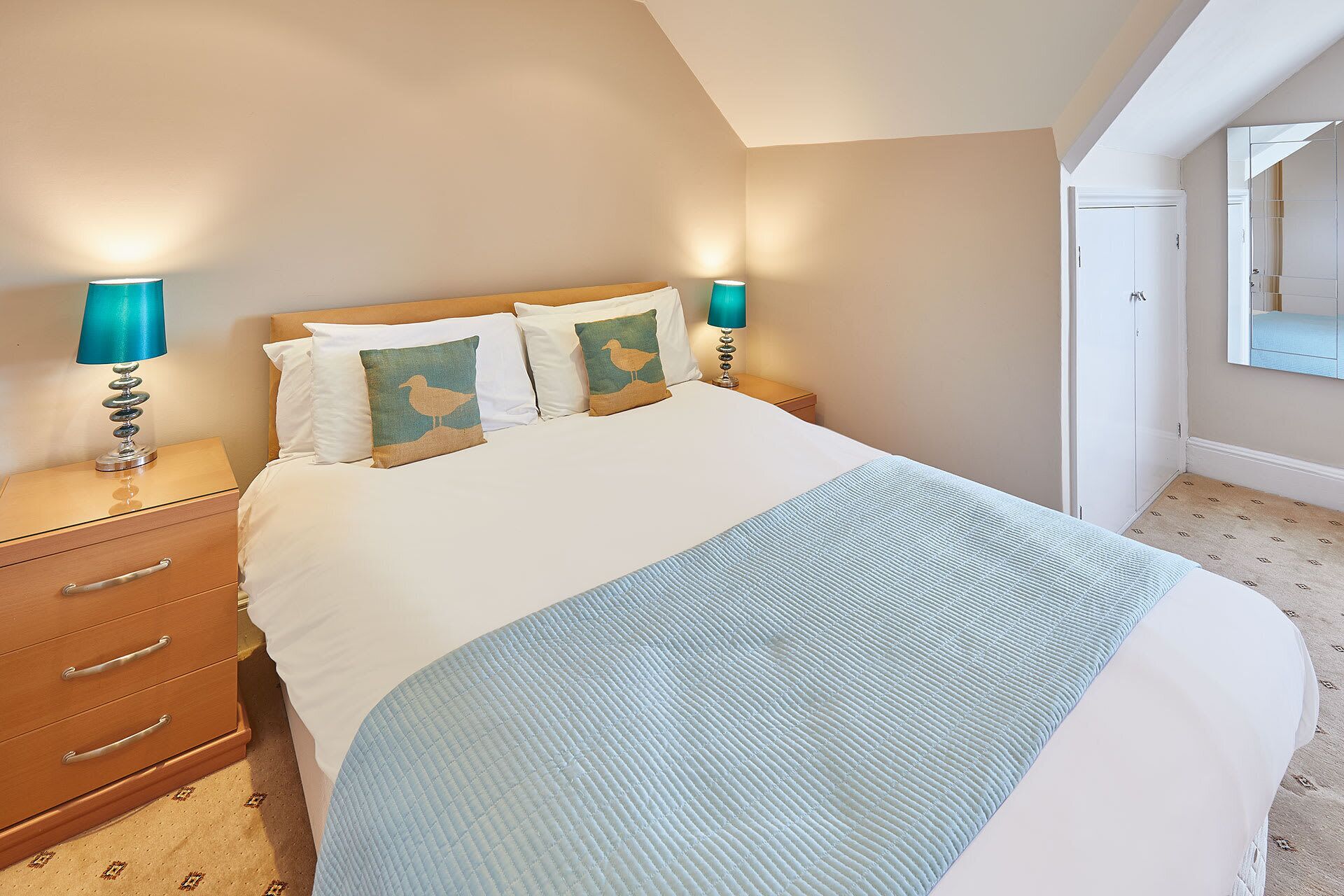 A neatly made bed with two pillows, a bedside table with a lamp, and a dresser with drawers.