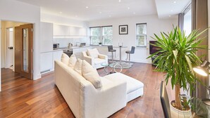 Ein modernes Wohnzimmer mit Sofa, Essbereich mit Tisch und Stühlen, Küche mit weißen Schränken und einem großen Fenster.