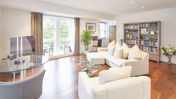 Ein modernes Wohnzimmer mit einem Glastisch, einem weißen Sofa und einem Bücherregal voller Bücher.