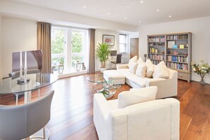 A modern living room with a glass coffee table, a white sofa, and a bookshelf filled with books. - Host Stay One Love (Harrogate)