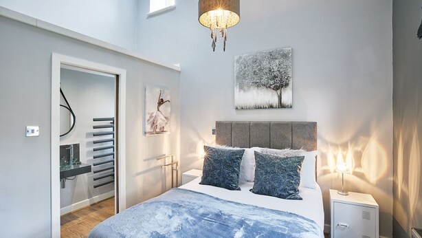 Une chambre à coucher avec un grand lit, une table de chevet, une commode, un lustre et des œuvres d’art accrochées aux murs.