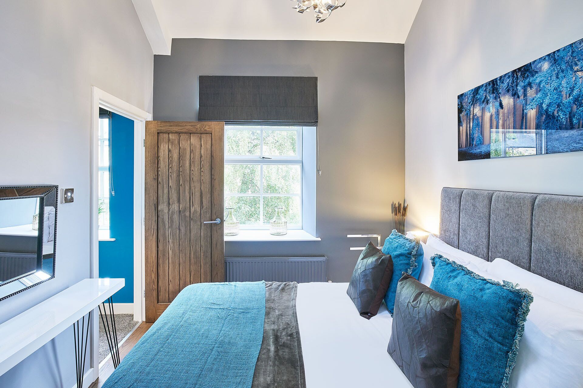 Een slaapkamer met een groot bed, een raam, een schilderij en een spiegel.