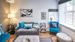 Un salon moderne avec un canapé gris, des fauteuils bleus, une table basse et des œuvres d’art accrochées aux murs.