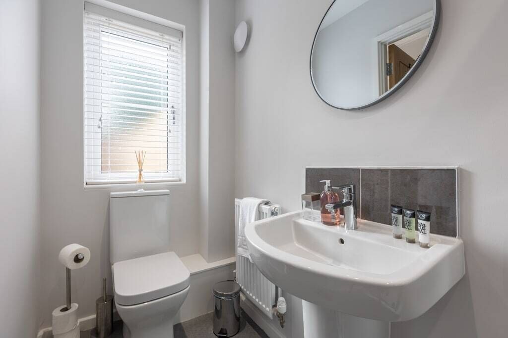 Un baño moderno con inodoro, lavamanos y ventana con persianas.