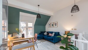 A modern living room with a blue sofa, a dining table with chairs, and a large plant.