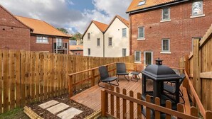 A backyard with a wooden deck, two chairs, a barbecue grill, and a wooden fence.