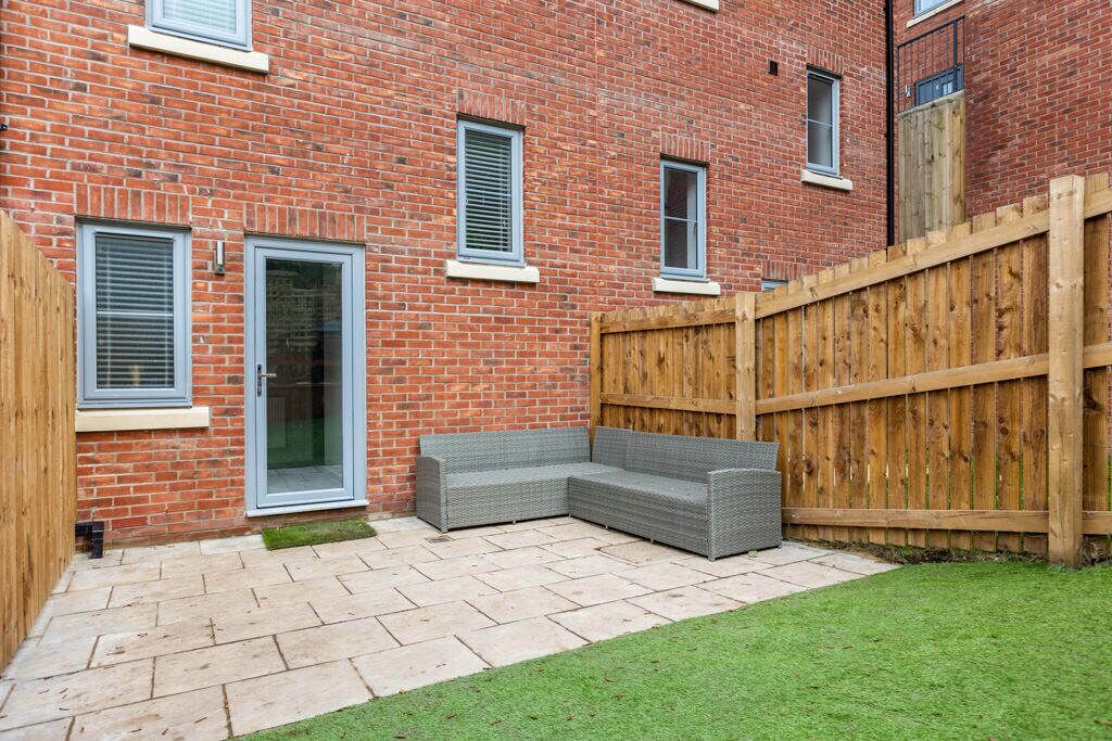 A brick building with a wooden fence, a grey outdoor seating area, and a door with glass panels.