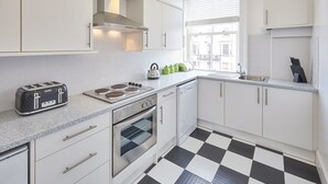 Eine moderne Küche mit weißen Schränken, einem schwarz-weißen Schachbrettboden, einem Toaster, einem Wasserkocher und einem Fenster mit Jalousien.
