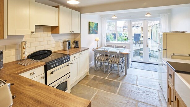 A modern kitchen with white cabinets, a wooden countertop, a stove, and a dining area with a table and chairs. - Host Stay Willow Cottage (York)