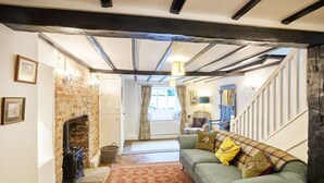 A cozy living room with exposed beams, a fireplace, a green sofa, and a patterned rug. - Host Stay Willow Cottage (York)