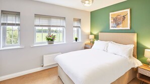 A bedroom with a large bed, two windows with blinds, a radiator, a green accent wall, and a framed picture of a bull.