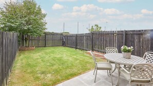 A backyard with a wooden fence, a grassy lawn, and a round table with chairs.
